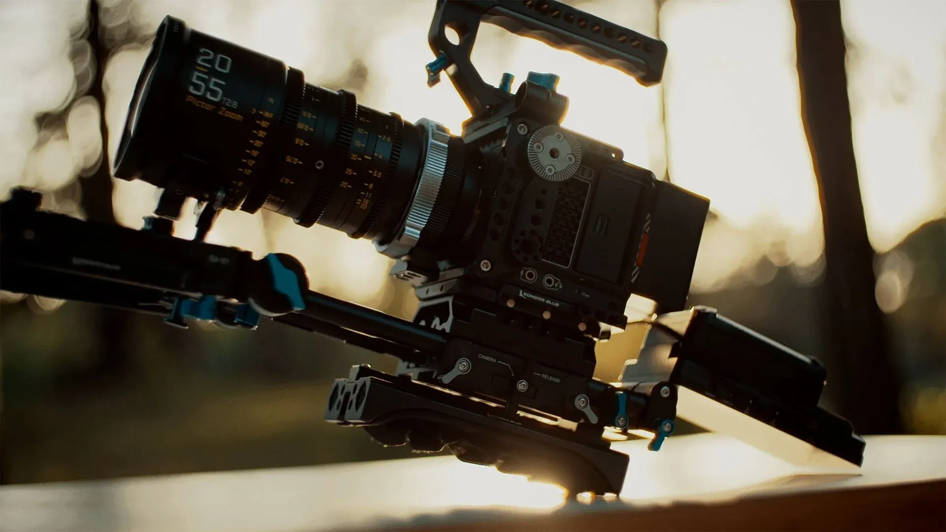 Close-up of the shoulder setup: camera, cine zoom lens, rods and shoulder pad backlit by the sun