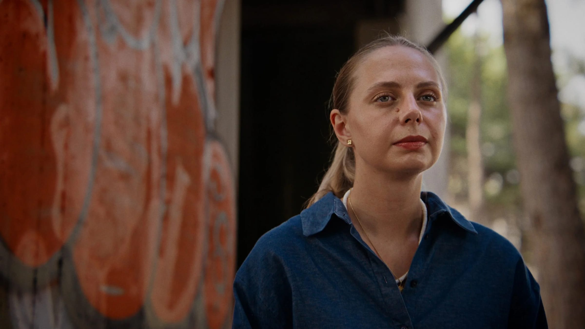 Close-up of the same woman at the right of the frame looking toward the left, graffiti wall right behind her