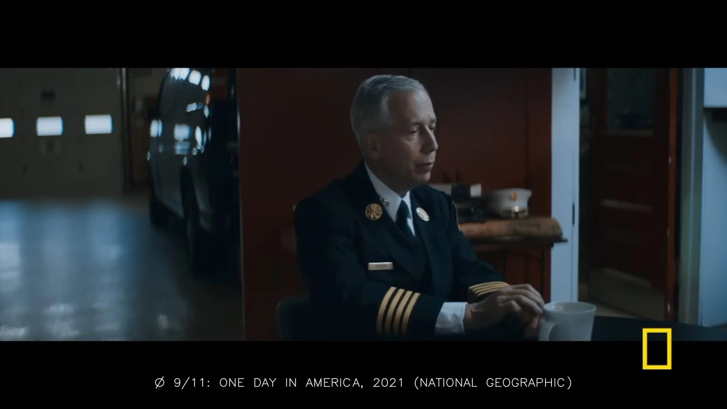 Frame from “9/11: One Day in America”: a fire captain seated at a table, filmed from a wide angle on the side