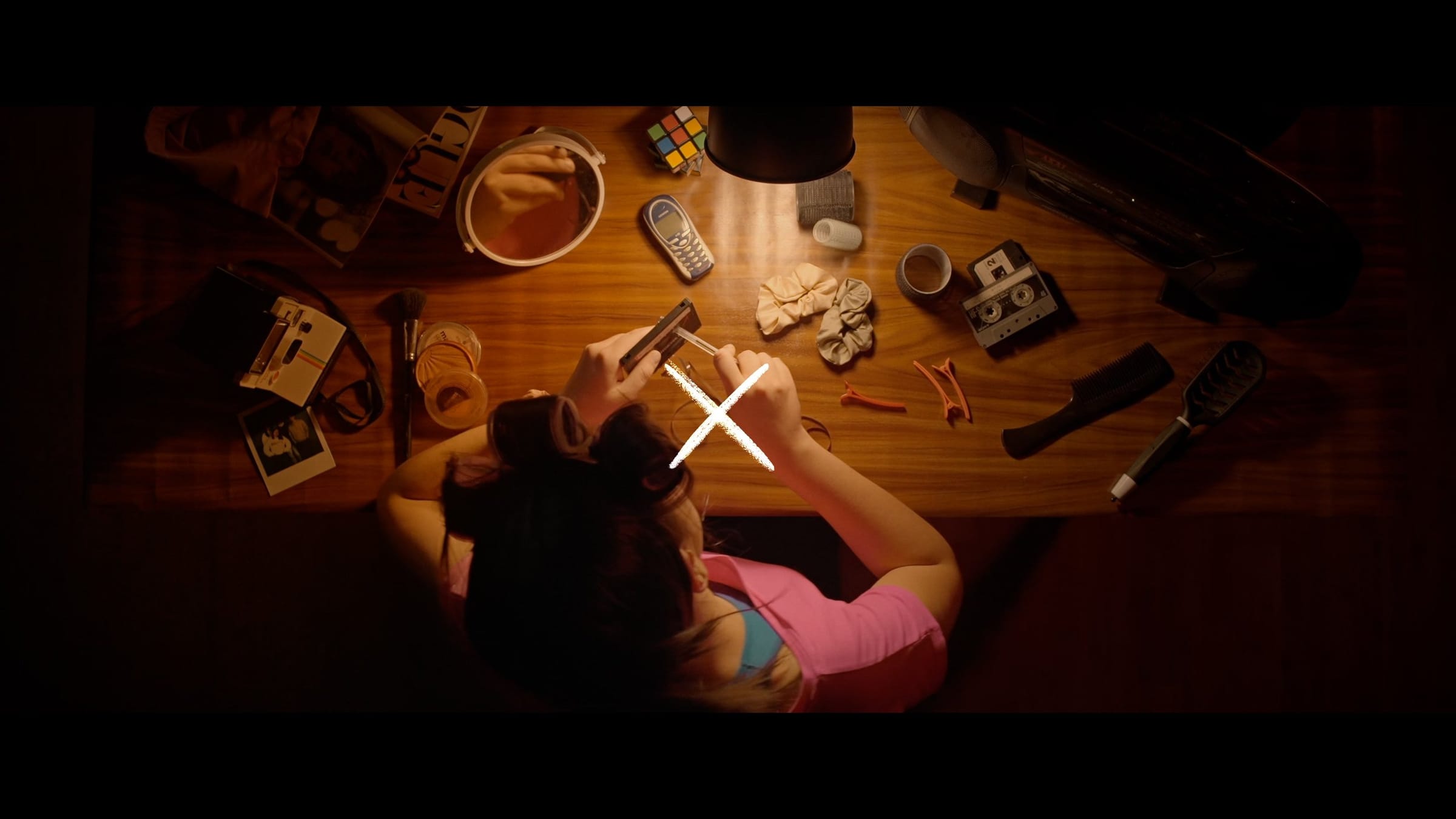 Overhead shot of a woman at a lamp-lit desk, a cross marking the action in the centre of the frame