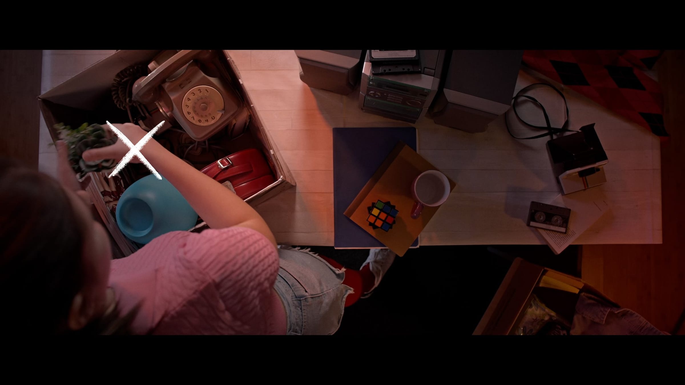 Overhead shot of a girl taking a plant out of a box, a cross marking the action on the left
