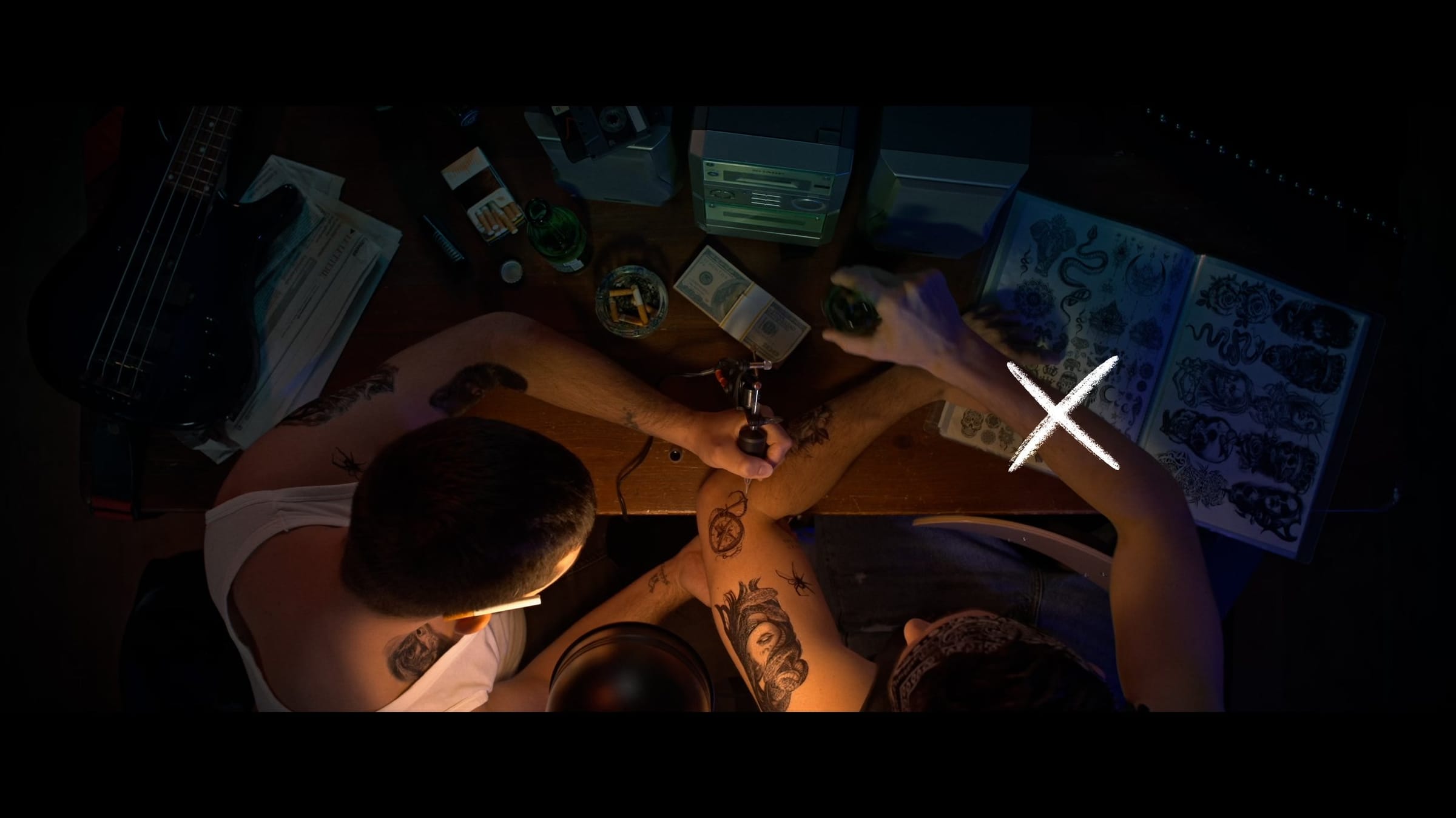 The tattoo scene, a cross marking a hand lifting a beer on the right of the frame
