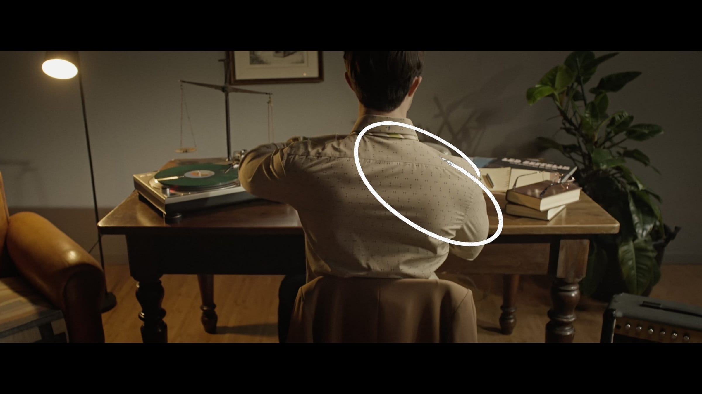 Opening shot: a man seen from behind at a desk with a turntable, a circle marking the light falling on his shoulder